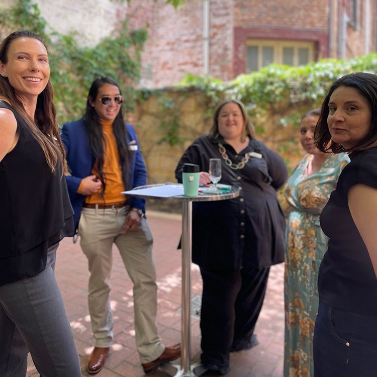 Vanessa and colleagues standing around a high table in a courtyard during the daytime at a Leadership WA event.